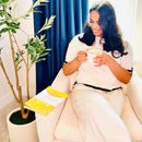 Woman sitting on a chair holding a mug looking down at the Happiness Prompted Journal next to her.