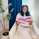 Woman sitting in a chair holding an Inspiration Prompted Journal with a plant and window in the background