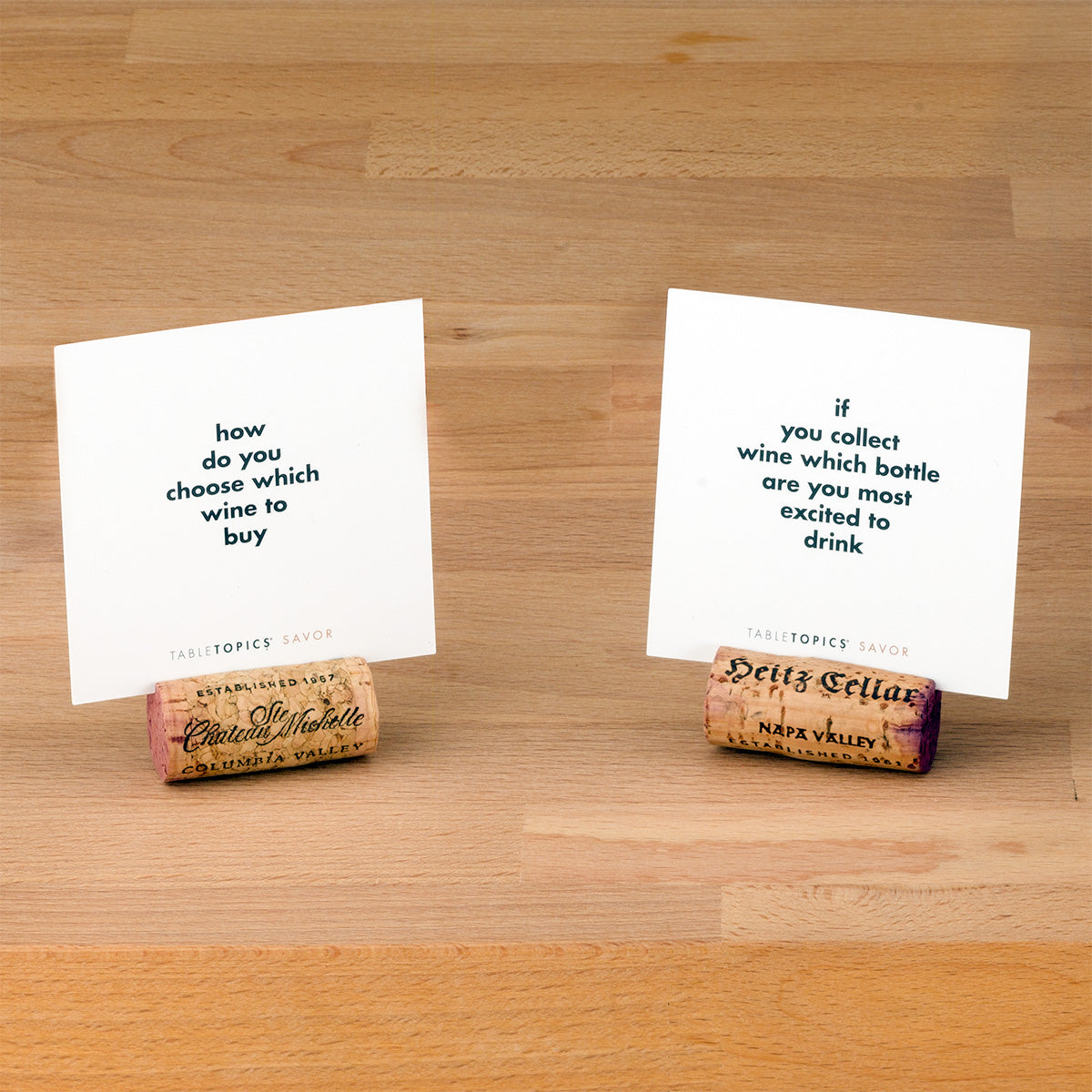 Two wine corks holding up two TableTopics Savor conversation cards