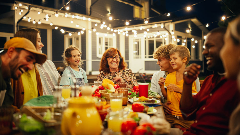 Family and friends enjoying a meal together outdoors at night with string lights.