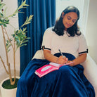 Woman sitting on a chair with a blanket on her lap, writing in the Gratitude Prompted Journal 