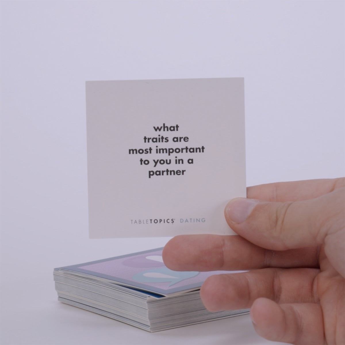 Hand pulling out TableTopics Dating conversation cards from the container and showing the questions